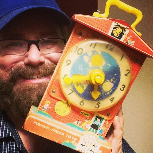 a man with glasses holding a cardboard toy with a clock in it