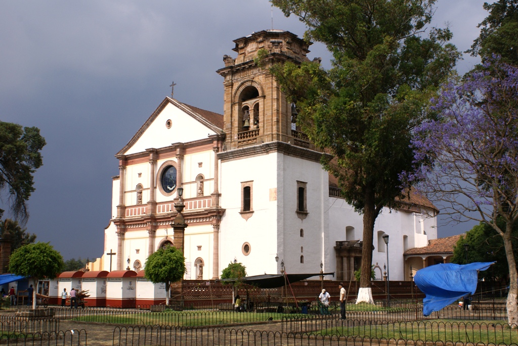 an old white church with a large window surrounded by trees