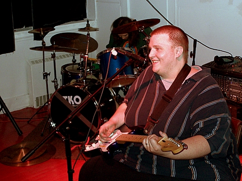 man playing guitar inside while another plays on the other side