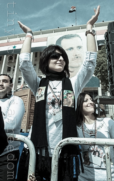 two women are holding their arms up, standing in front of some people and a poster