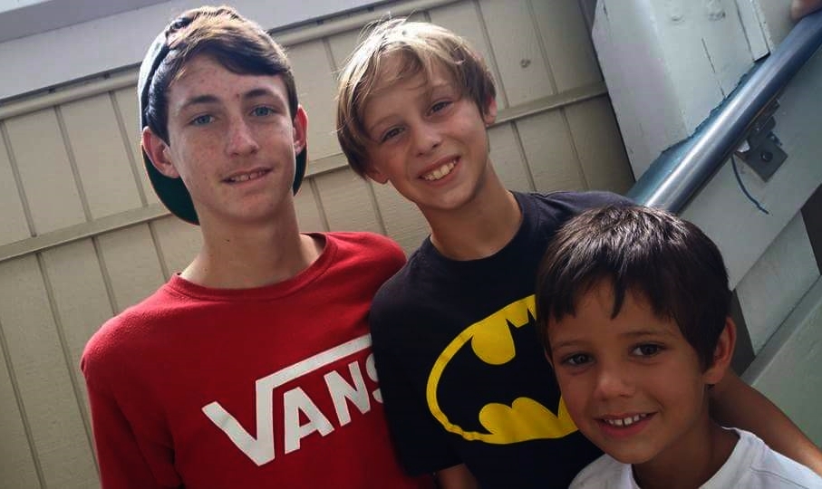 three boys, two wearing batman masks, pose for a po