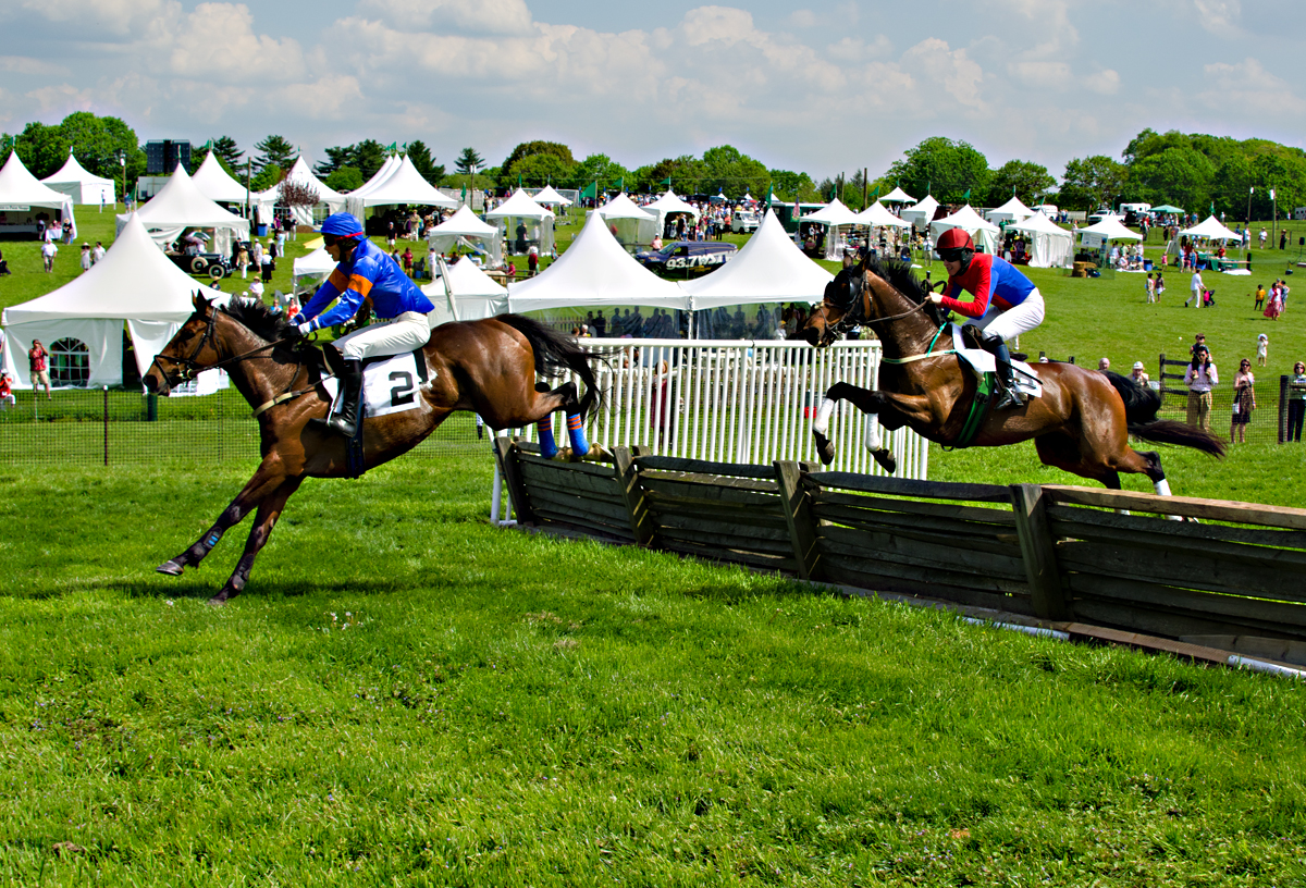 two men on horses are riding by the fence