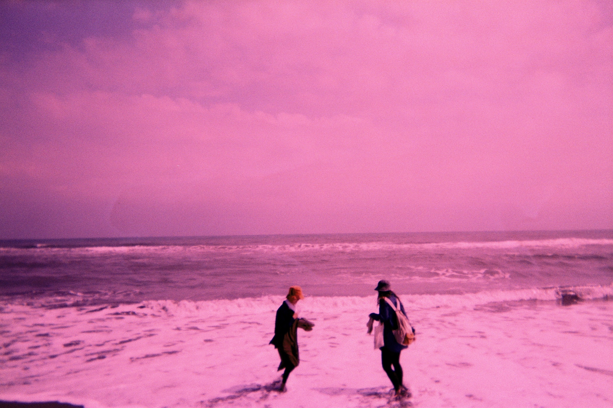 two people are walking through the surf holding surf boards