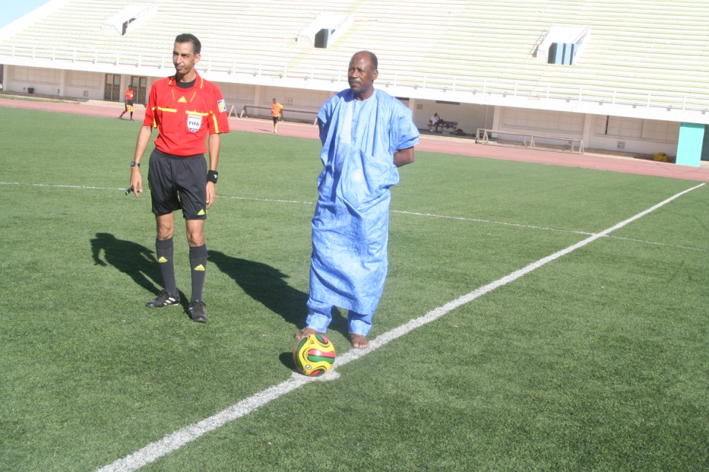 a man kicking a soccer ball while standing next to another man