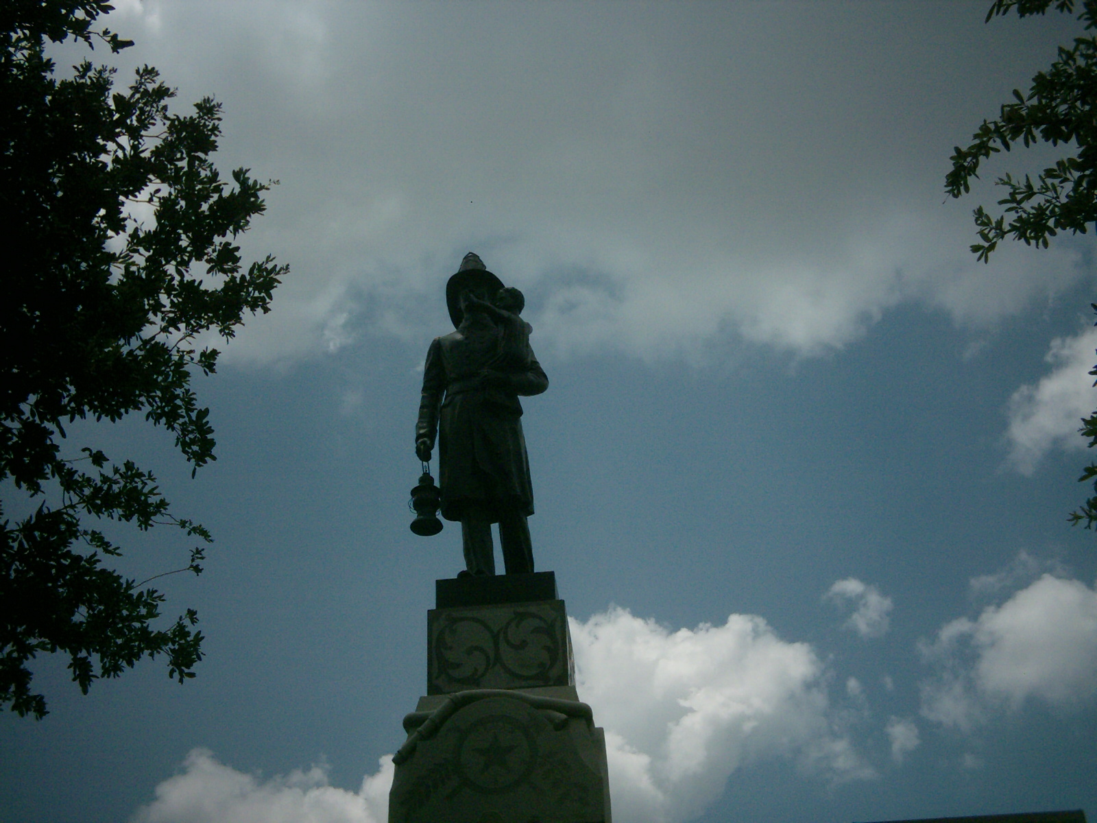 a statue stands in the clouds above some trees