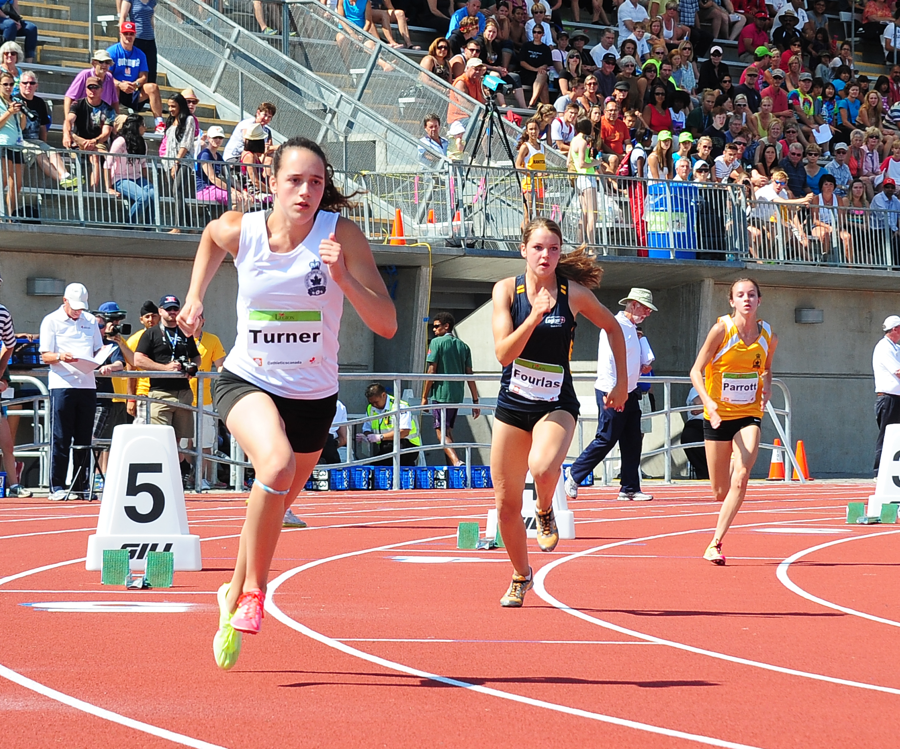 runners compete at an outdoor track with large audience in the stands