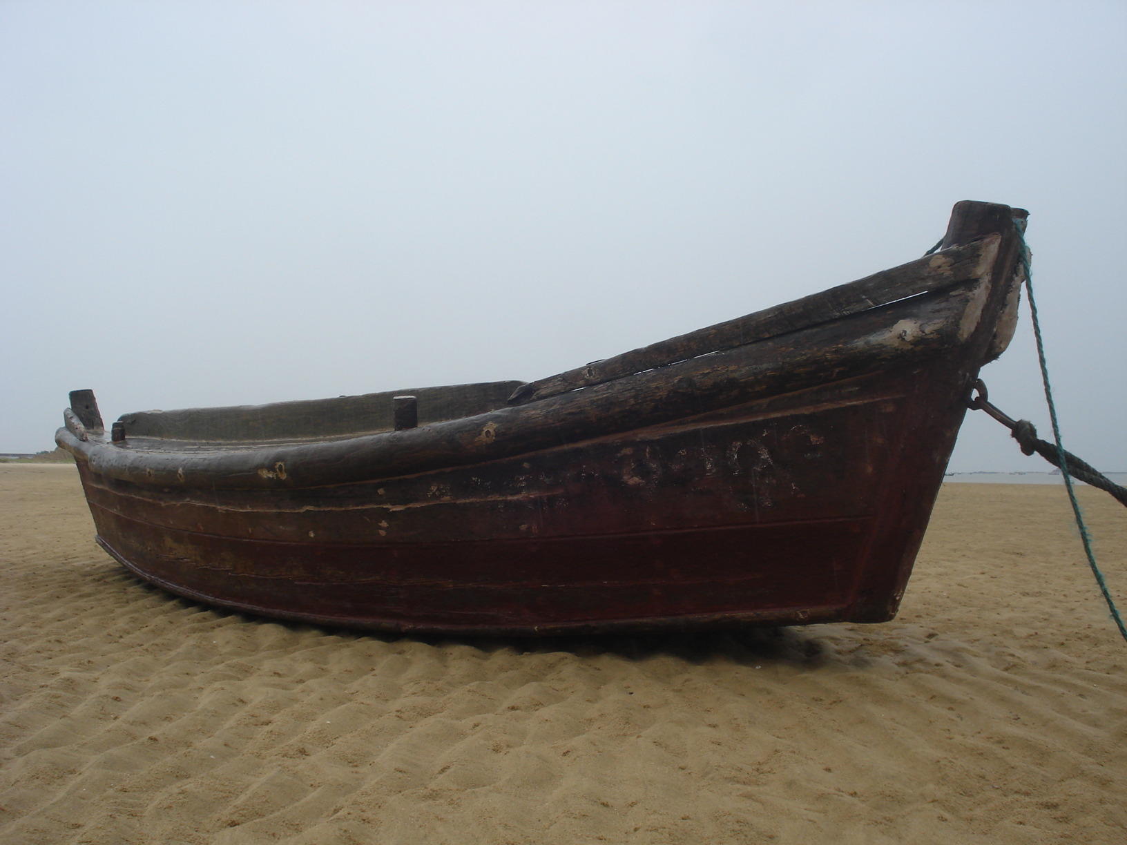 a rusted up boat laying in the sand on the beach