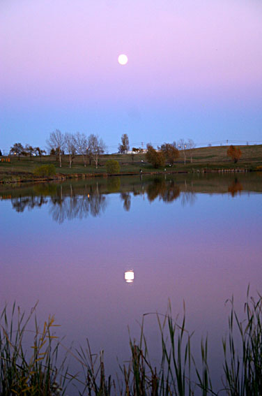 the moon is setting above a calm lake
