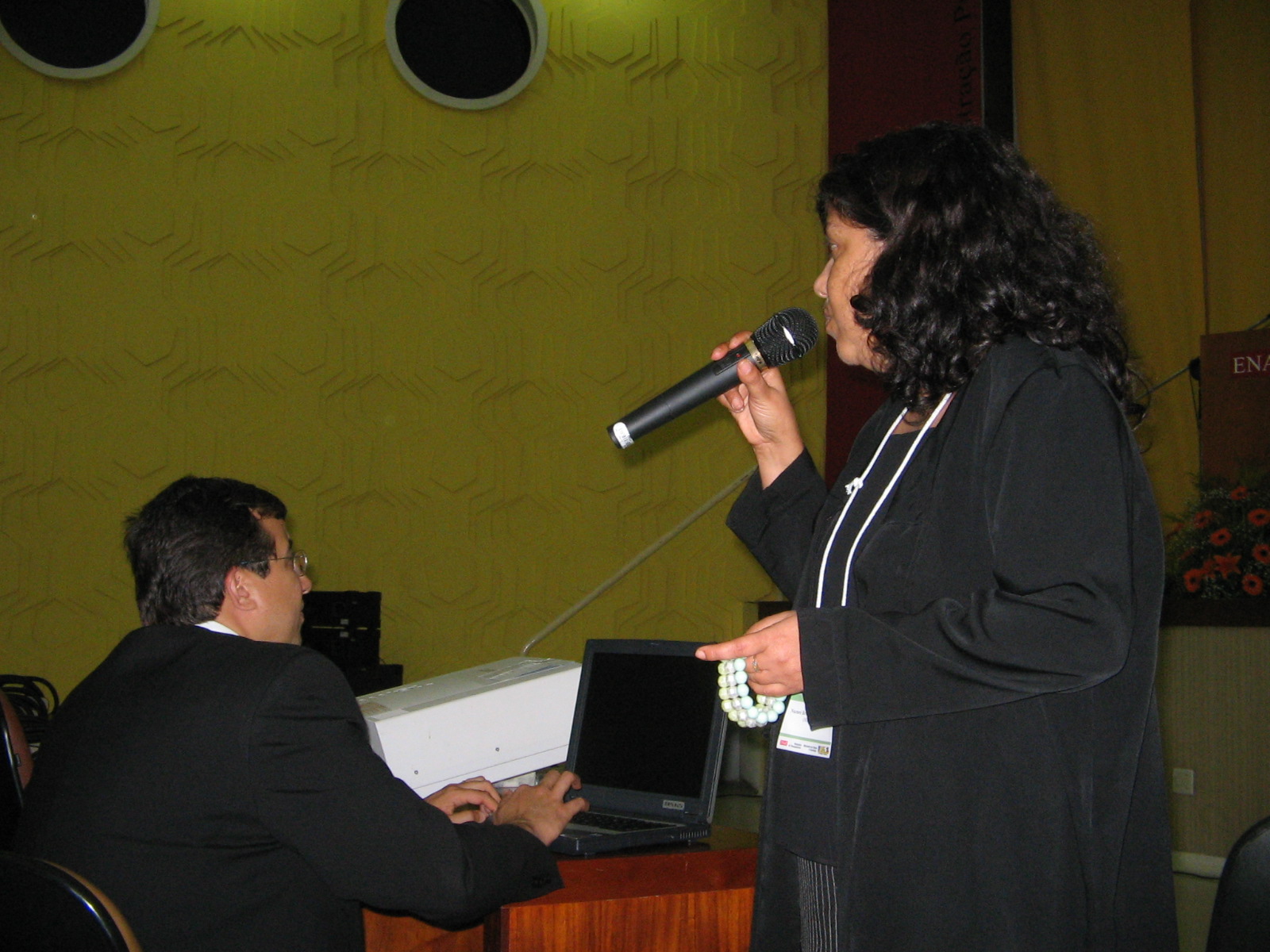 a woman on a microphone speaking into a man in a black suit