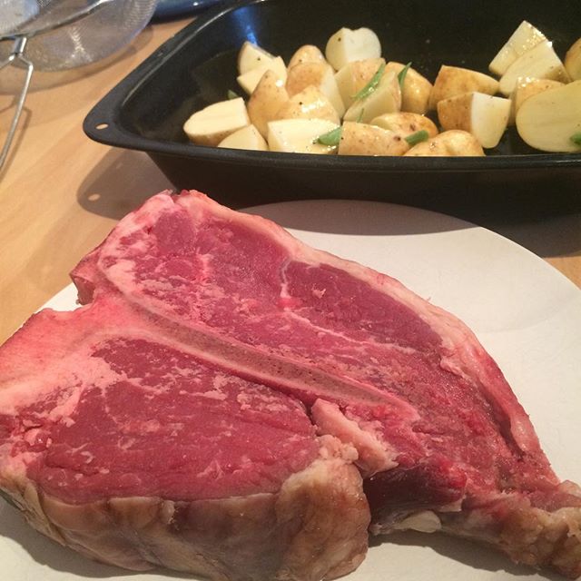 two steaks, potatoes and a pan of meat are sitting on the table