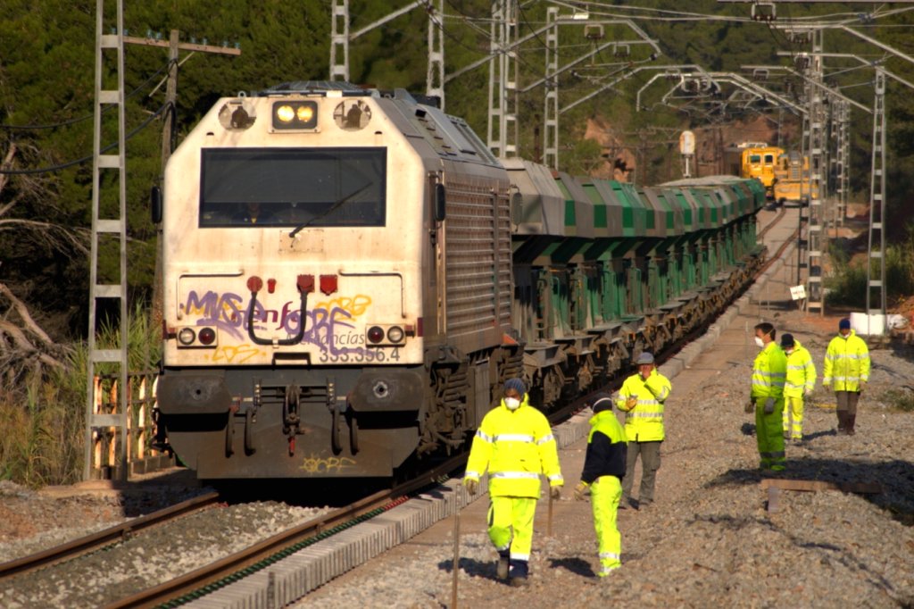 trains and men in yellow uniforms walk down the tracks