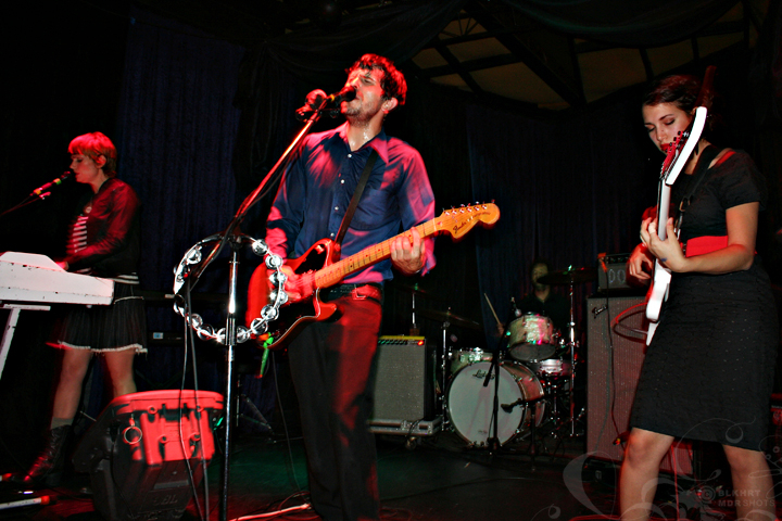 three people standing near a microphone and two with guitars