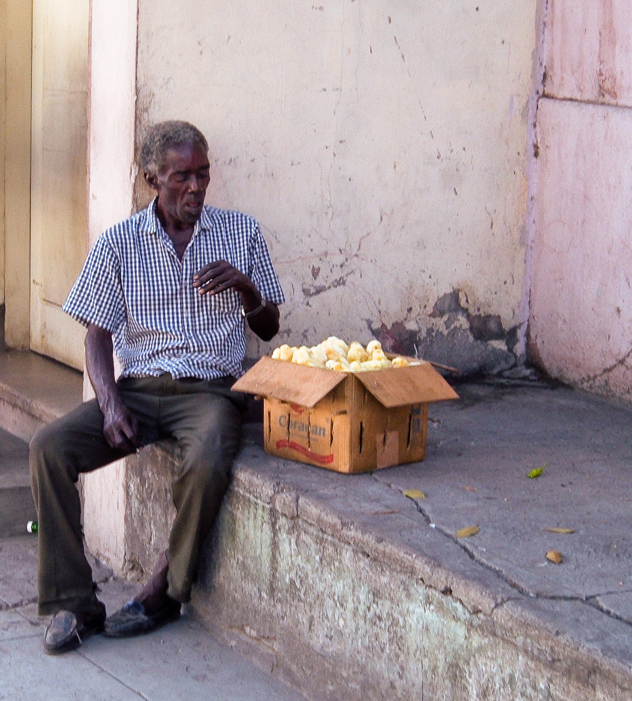 an elderly man sitting at the edge of a wall eating a pizza