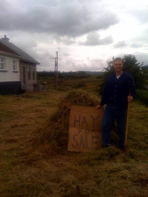 a man standing in the grass holding a sign that reads hay sale