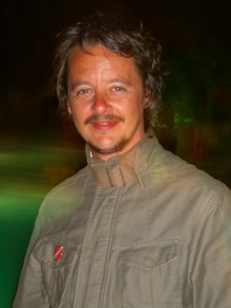 a man with a mustache smiles as he stands in a dark room