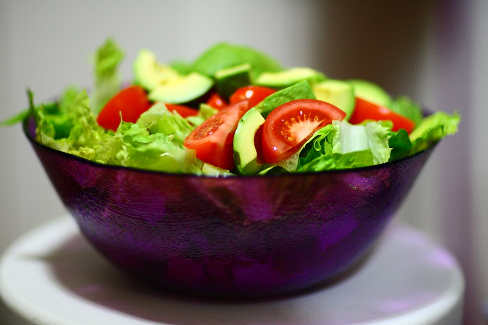 a purple bowl full of salad with avocado and tomatoes on top