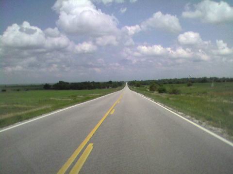 an empty highway with yellow painted lines and some clouds