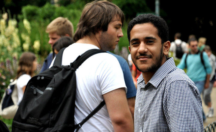 a young man with a beard smiling while another stands next to him