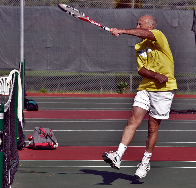 an elderly man in action on a tennis court