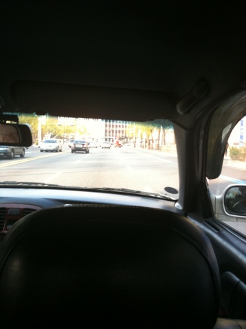 view from inside the car showing on street and building, and cars with one person's head up in the driver's seat