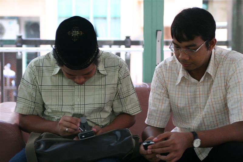 two men sitting on a couch looking at their cell phones