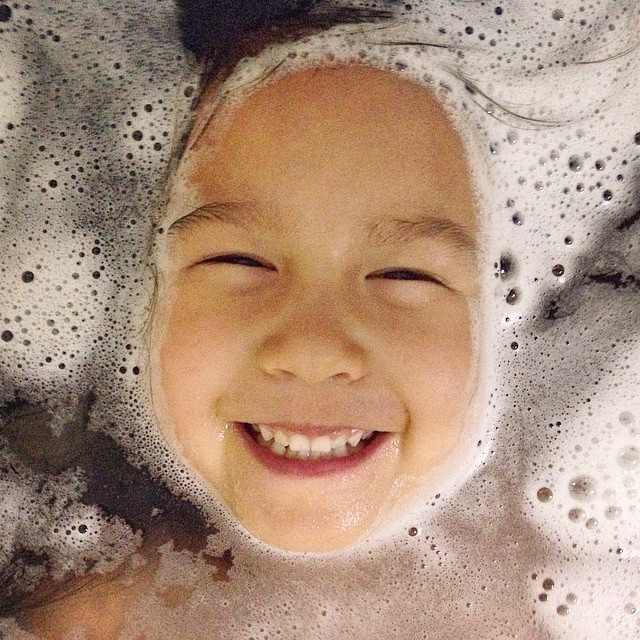 a child laying in bubbley water with a smile