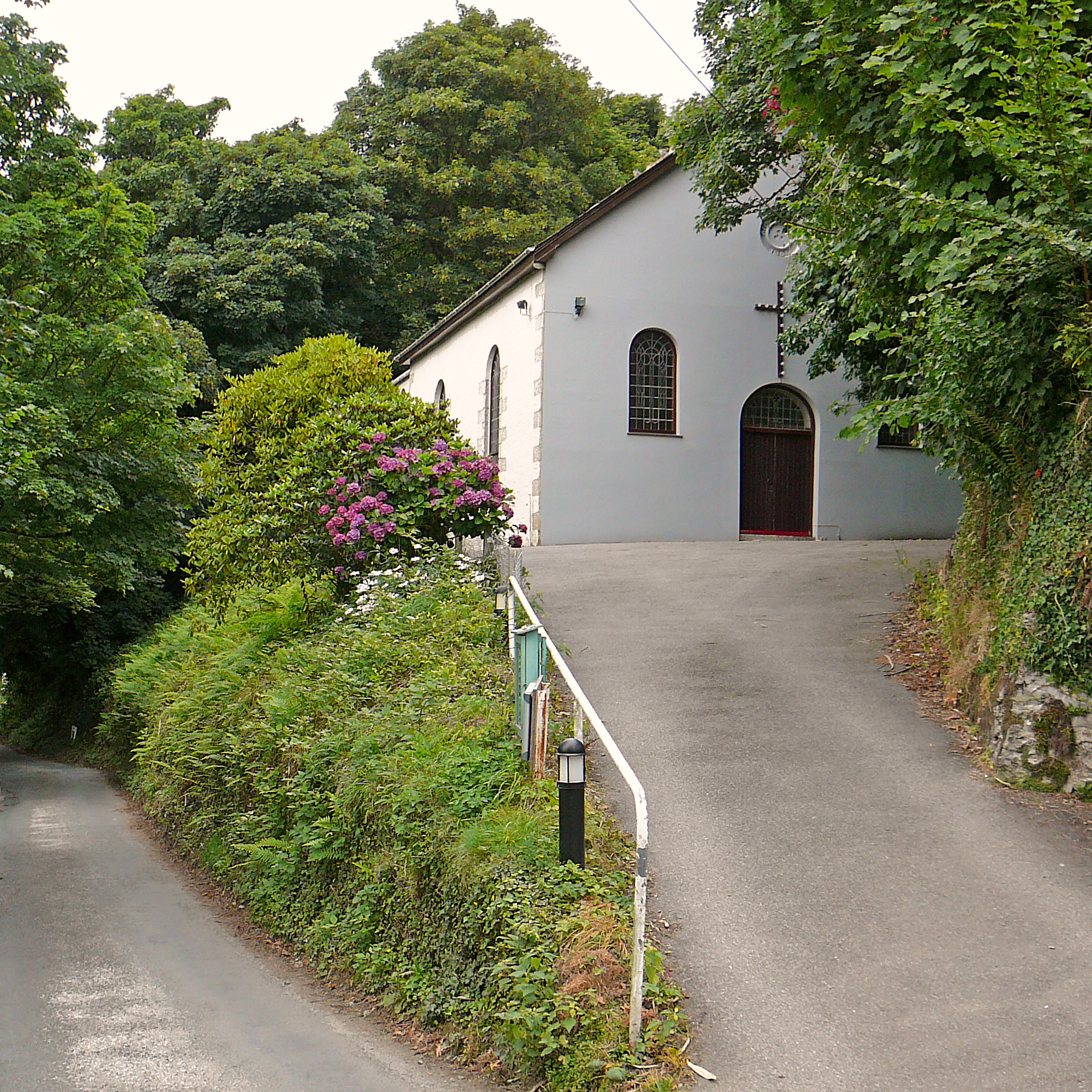 a small church with a driveway going through some trees