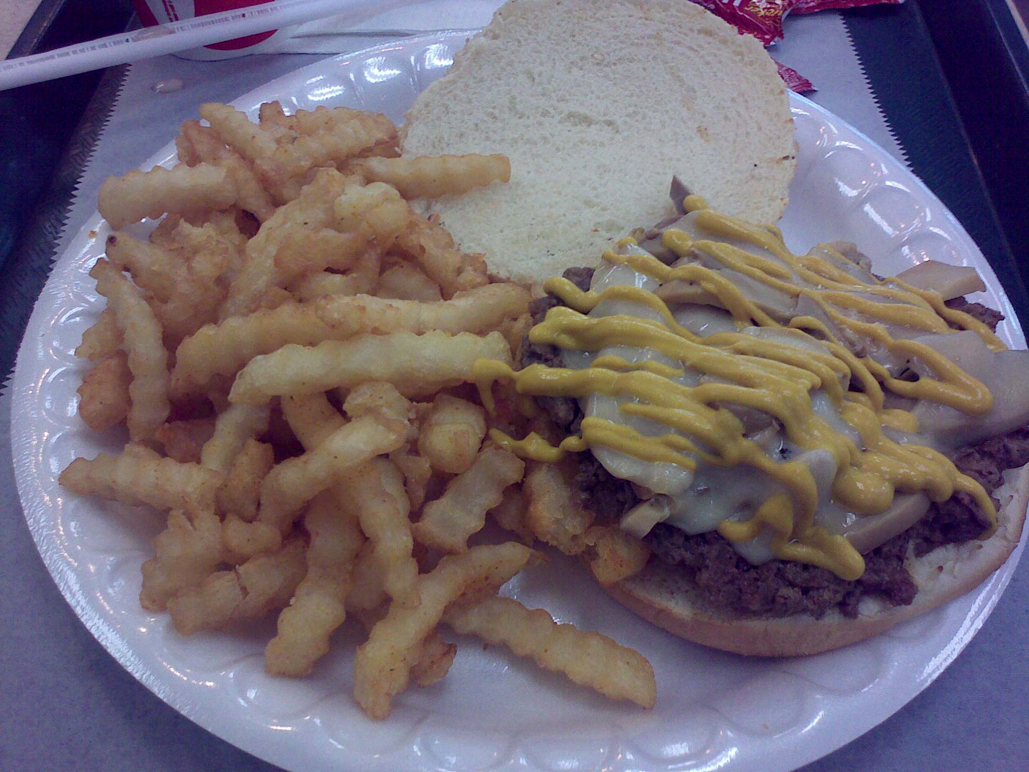 a burger with mustard and gravy is on a paper plate next to french fries