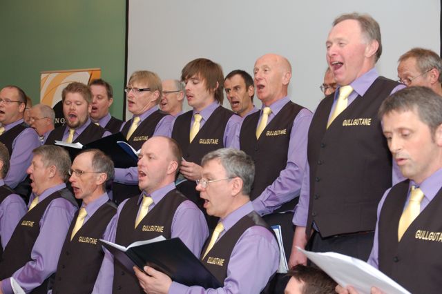 an choir is shown singing with one person holding a sheet