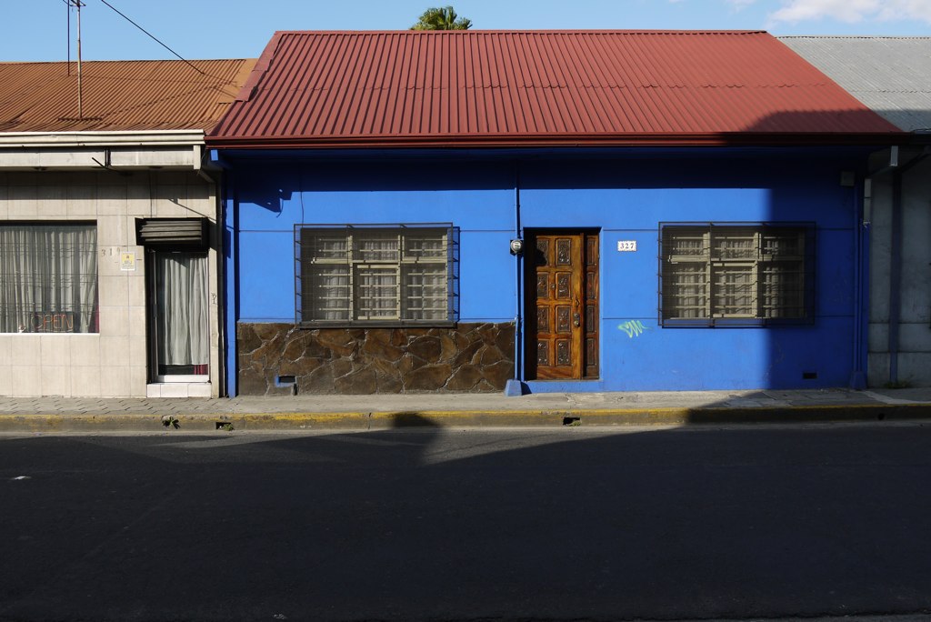the street has two buildings, one blue with a red roof and one white with windows