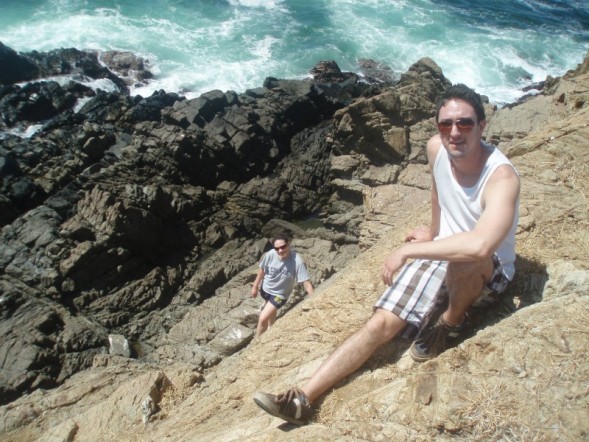 two people sit on rocky coast near ocean