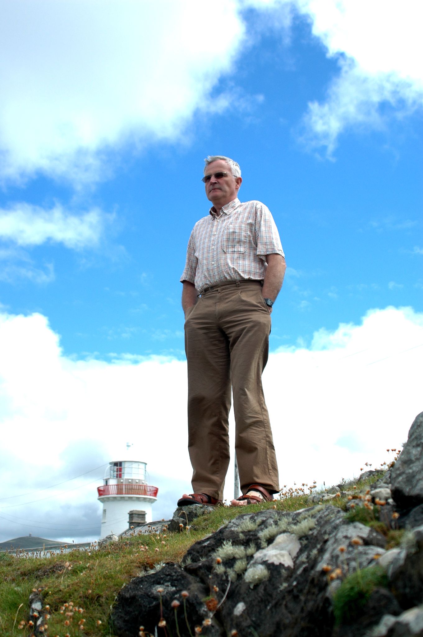 a man in khaki poses for a po with a lighthouse behind him