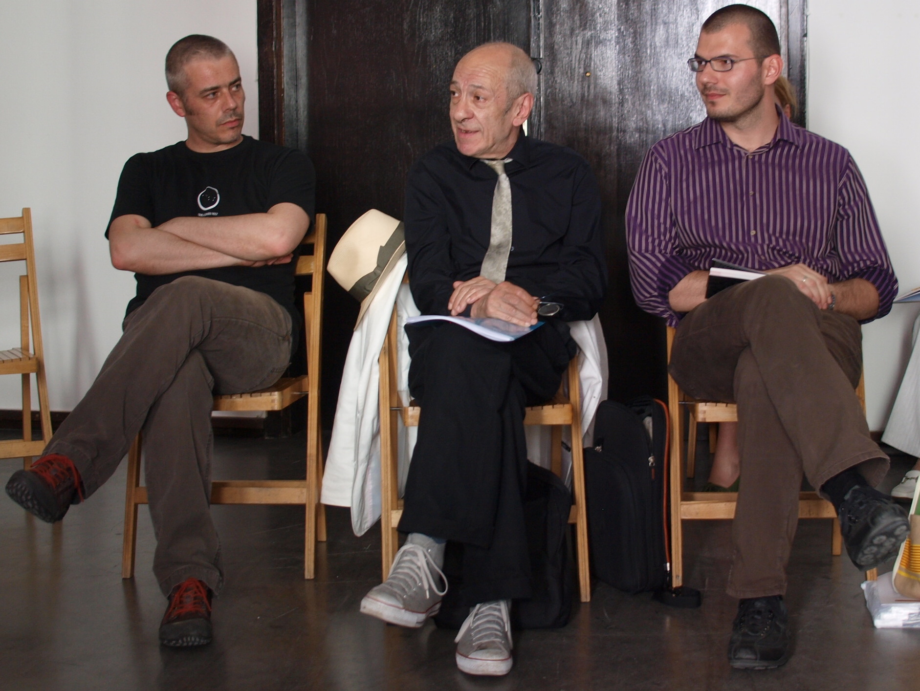 three men sitting next to each other on wooden chairs