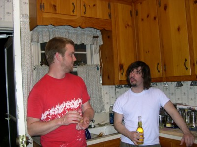 two men standing in a kitchen with food on the counter