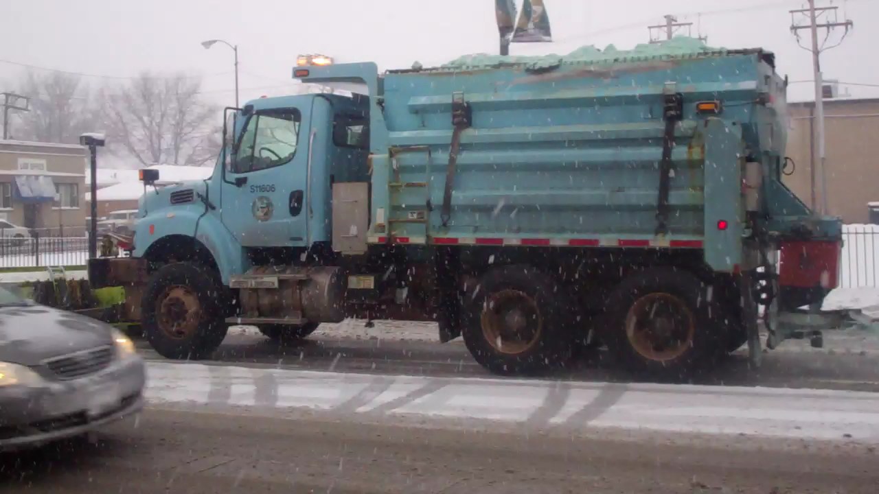 a blue dump truck driving down a street covered in snow