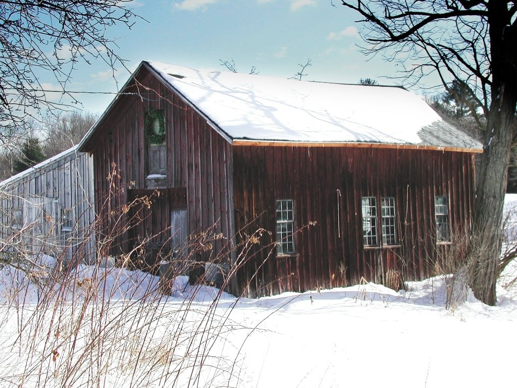 the large barn is covered with snow next to trees