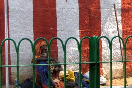 an older man sitting near a green fence