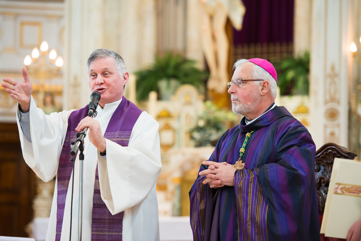 two priests are holding an empty microphone while one holds the microphone and the other holds his hands out