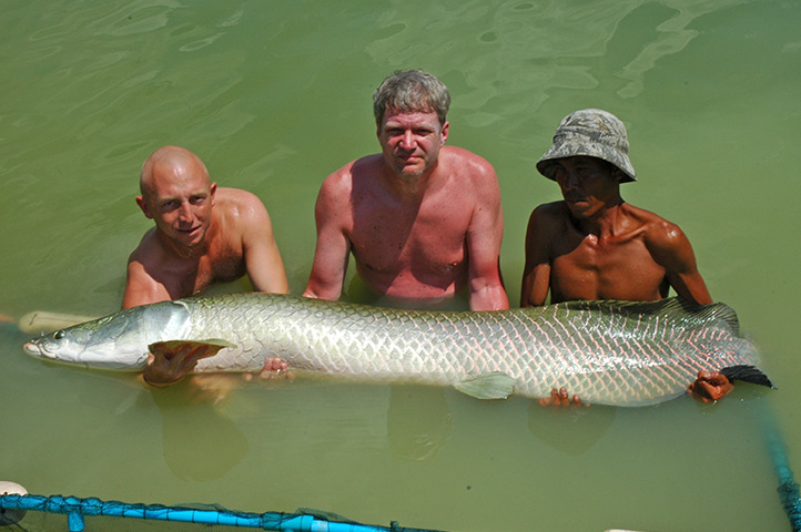 three people are swimming in the water and holding a large fish