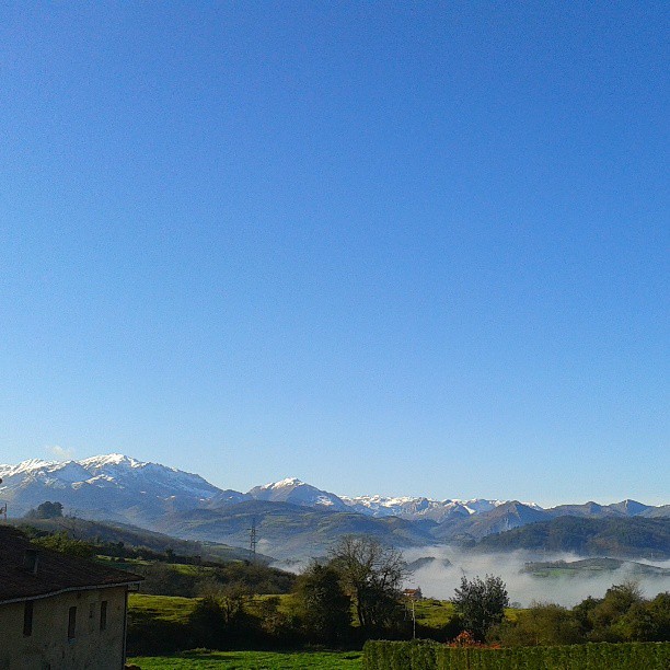 the mountains rise over a green field in front of some clouds