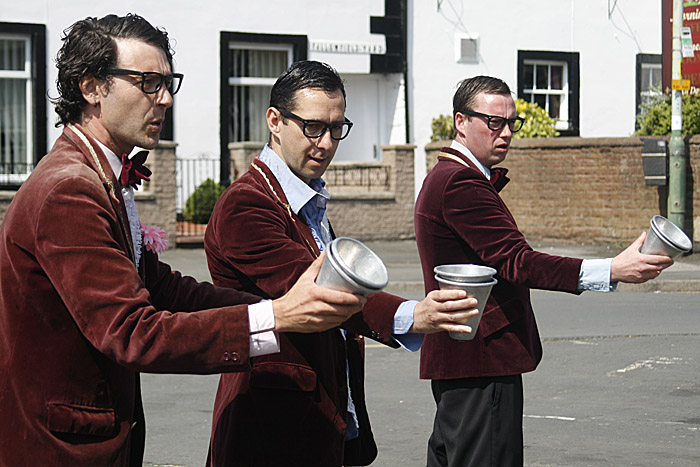 four men in red velvet blazers and ties on a street