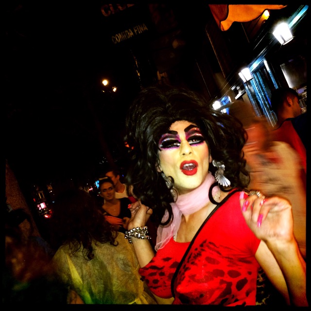 a woman with her face painted white and red and a red and black makeup is standing on the street in a crowd of people