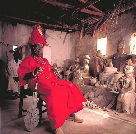 a red colored person sitting in a chair with a wooden mask and red dress