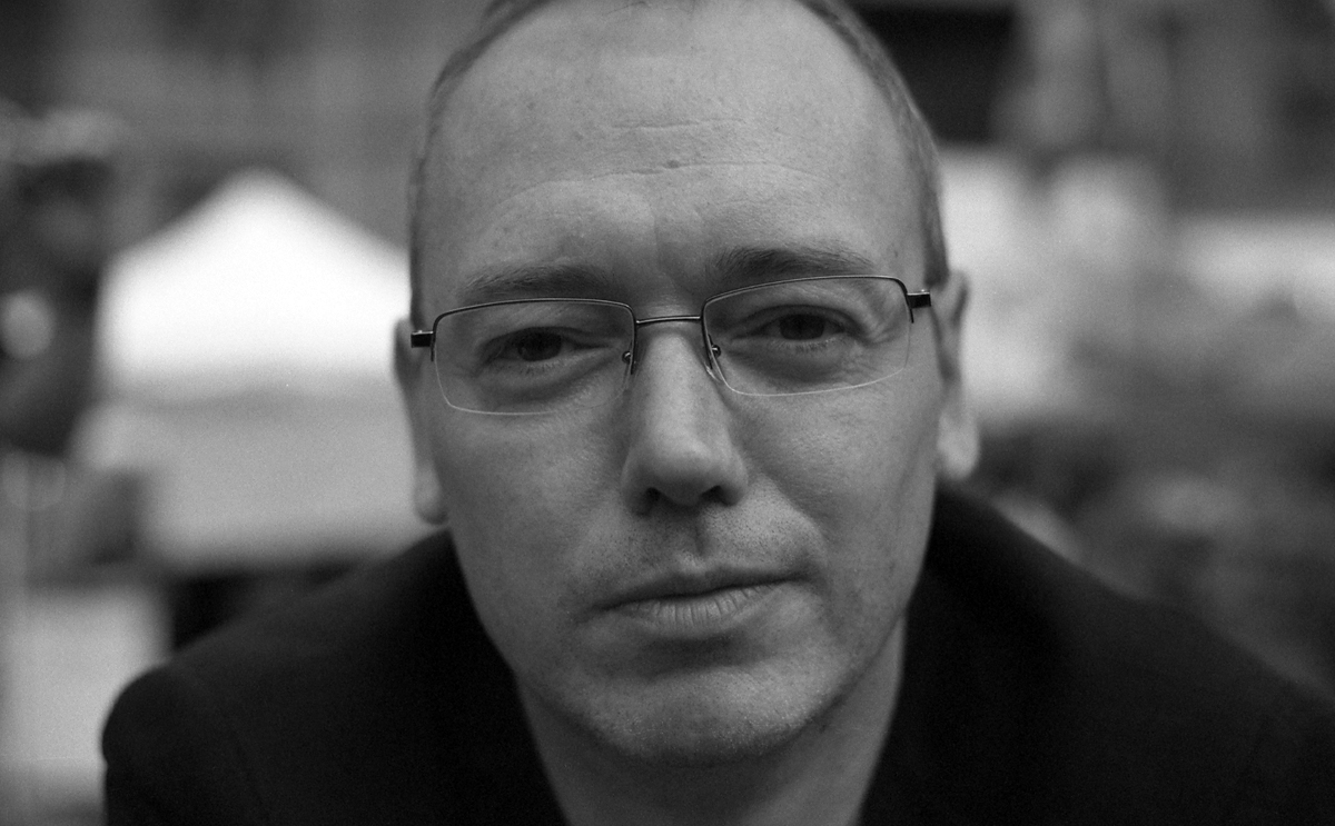 man wearing glasses in front of some buildings