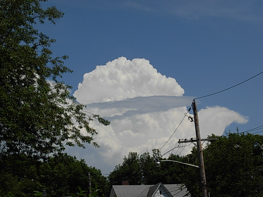 large cloud looming over a house with trees lining the side