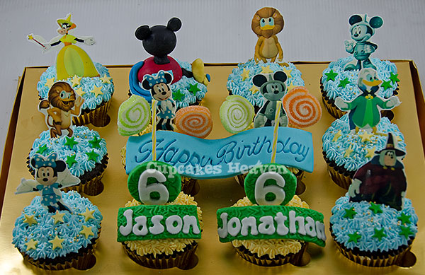 birthday cupcakes, including mickey mouse toppers, are displayed in front of a cake