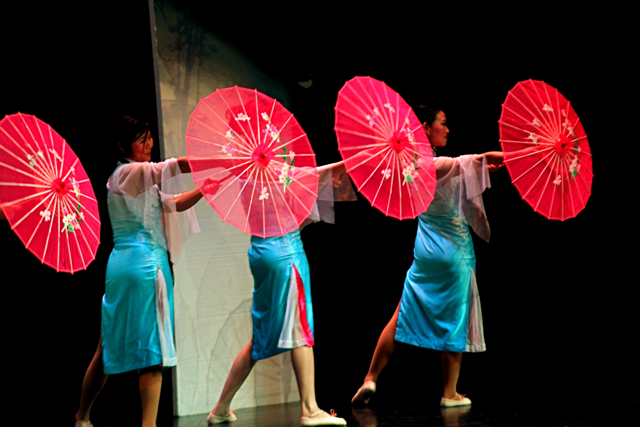four people in colorful outfits holding up red and pink parasols