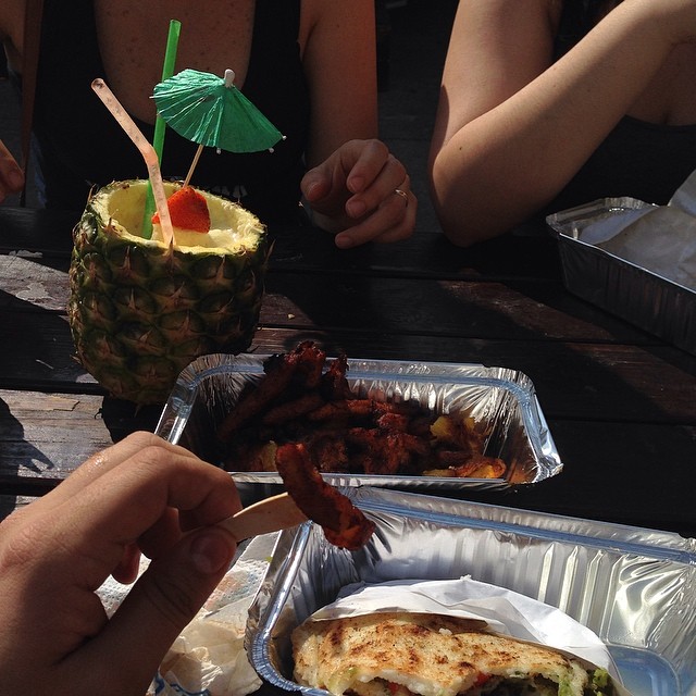 people are eating food from tinfoil trays and a pineapple drink in a bucket