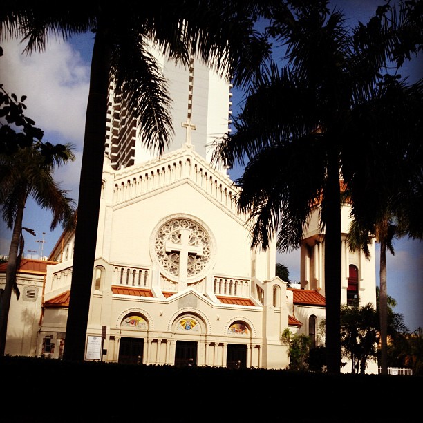 palm trees surround the front of a white church with two clocks on each side