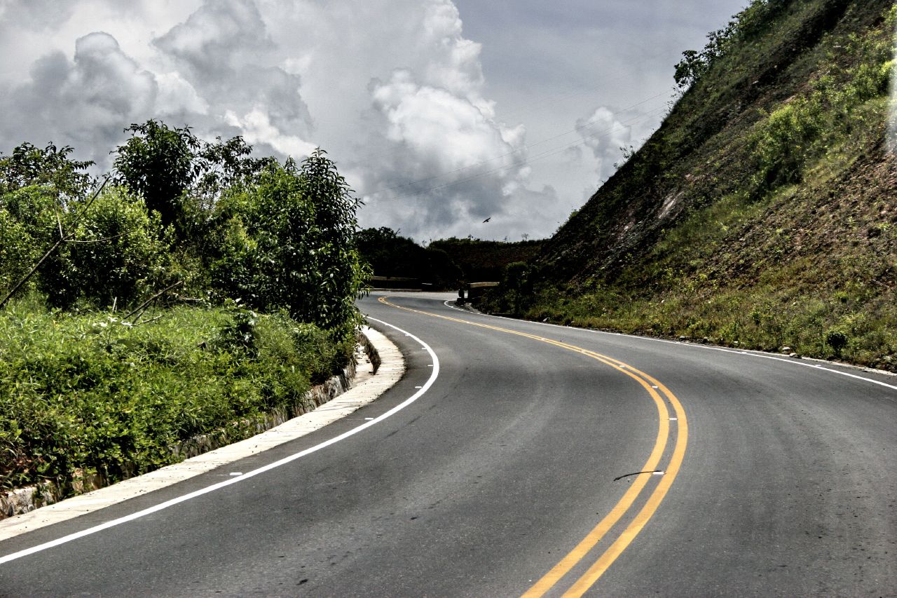 a curved road surrounded by green trees in the middle of a mountain